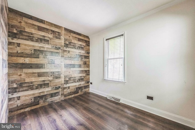 empty room featuring baseboards, dark wood-style floors, crown molding, and wooden walls