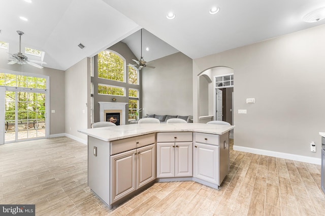 kitchen featuring a ceiling fan, open floor plan, arched walkways, a warm lit fireplace, and high vaulted ceiling
