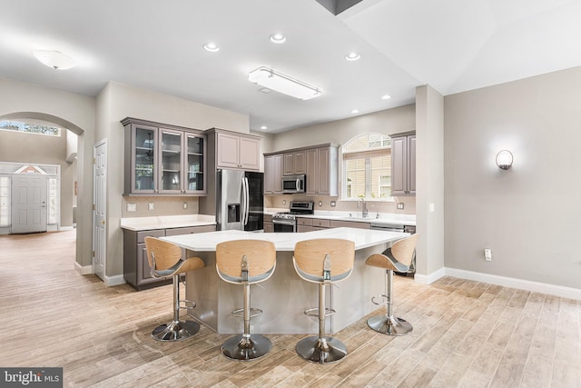 kitchen featuring stainless steel appliances, a sink, arched walkways, gray cabinetry, and a breakfast bar