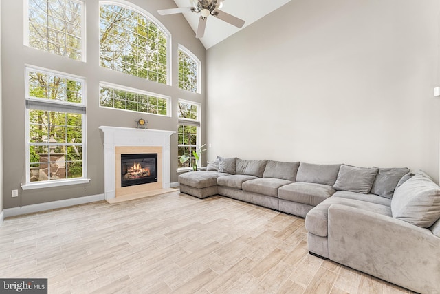 living area with high vaulted ceiling, a ceiling fan, a fireplace, wood finished floors, and plenty of natural light