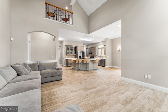 living room featuring arched walkways, light wood-style flooring, baseboards, high vaulted ceiling, and recessed lighting