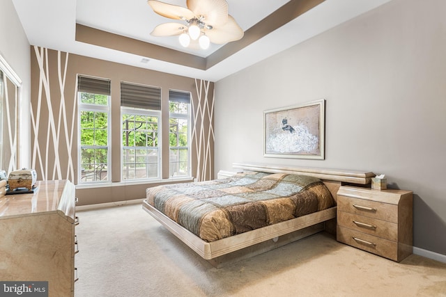 bedroom with light carpet, baseboards, a raised ceiling, and a ceiling fan