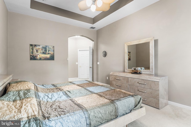 bedroom featuring arched walkways, carpet, a raised ceiling, baseboards, and ceiling fan