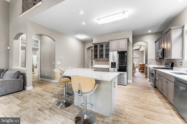 kitchen featuring appliances with stainless steel finishes, arched walkways, a sink, light wood finished floors, and recessed lighting