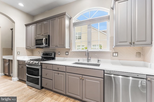 kitchen with appliances with stainless steel finishes, gray cabinets, a sink, arched walkways, and healthy amount of natural light