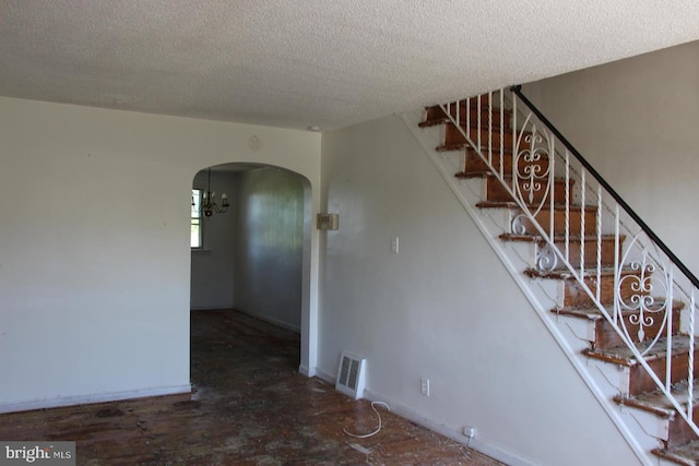 stairway featuring a textured ceiling, arched walkways, baseboards, and a chandelier