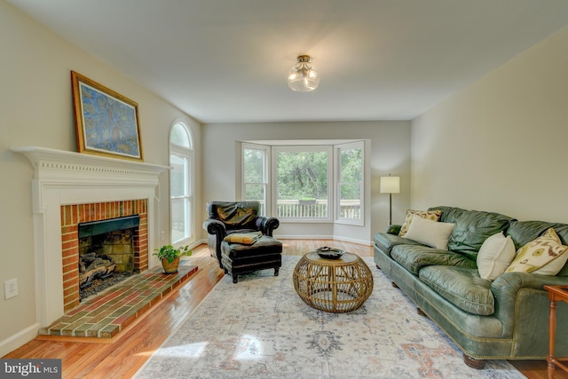 living room featuring wood finished floors, a brick fireplace, and baseboards