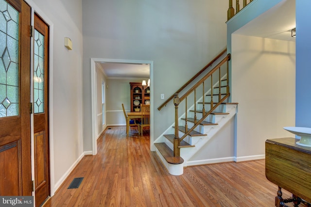 entryway with wood finished floors, stairs, baseboards, and crown molding