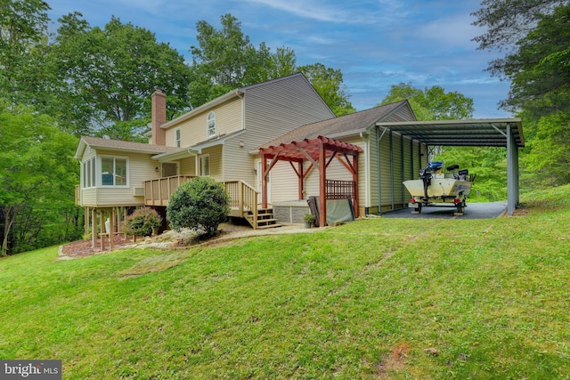 rear view of property featuring a lawn, a chimney, a wooden deck, a detached carport, and driveway