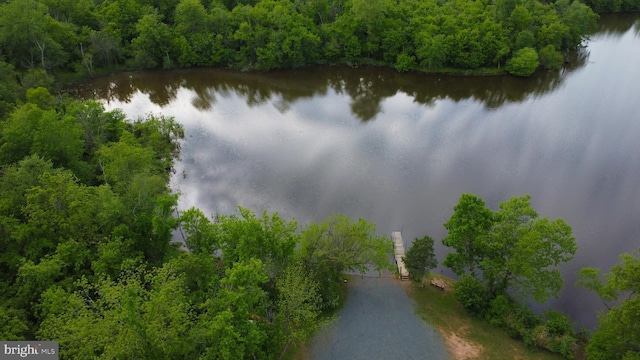 drone / aerial view of a nearby body of water and a heavily wooded area