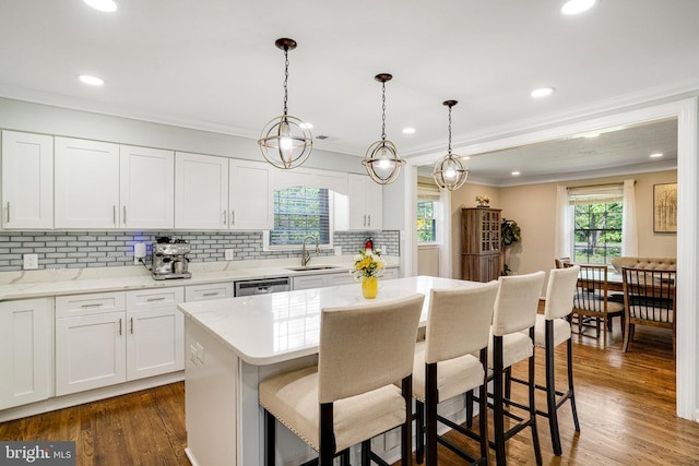 kitchen with a sink, a breakfast bar area, backsplash, stainless steel dishwasher, and crown molding