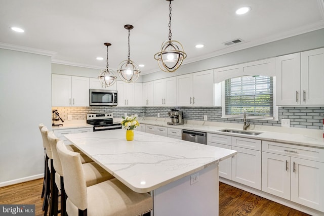 kitchen featuring stainless steel appliances, a sink, a center island, crown molding, and white cabinetry