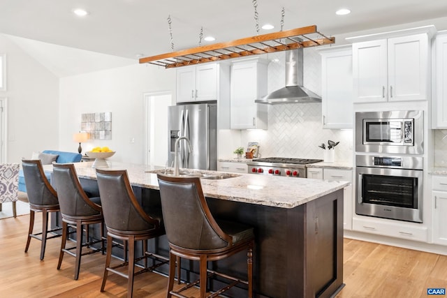 kitchen with appliances with stainless steel finishes, wall chimney exhaust hood, a sink, light wood-style floors, and recessed lighting