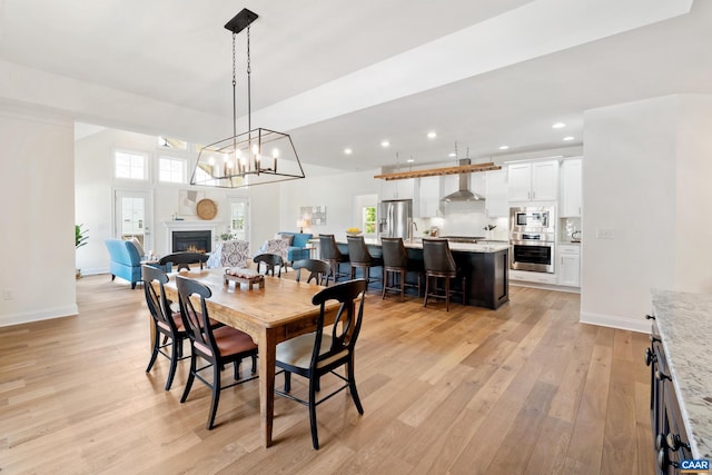 dining space featuring light wood-style floors, recessed lighting, a glass covered fireplace, baseboards, and a chandelier