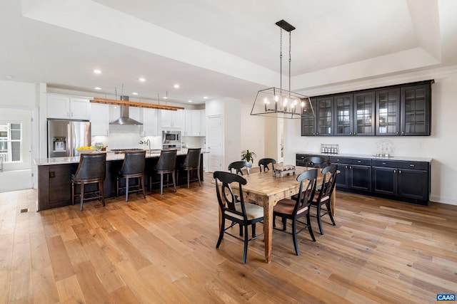 dining space with light wood-style floors, recessed lighting, a tray ceiling, and a chandelier