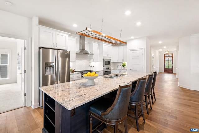 kitchen with wall chimney range hood, a sink, appliances with stainless steel finishes, recessed lighting, and white cabinets