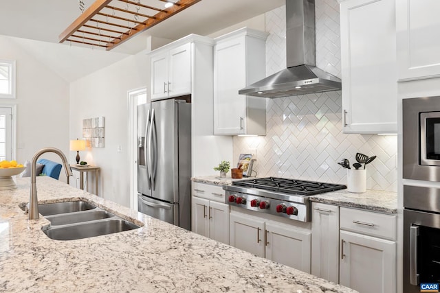 kitchen featuring stainless steel appliances, wall chimney range hood, a sink, and decorative backsplash
