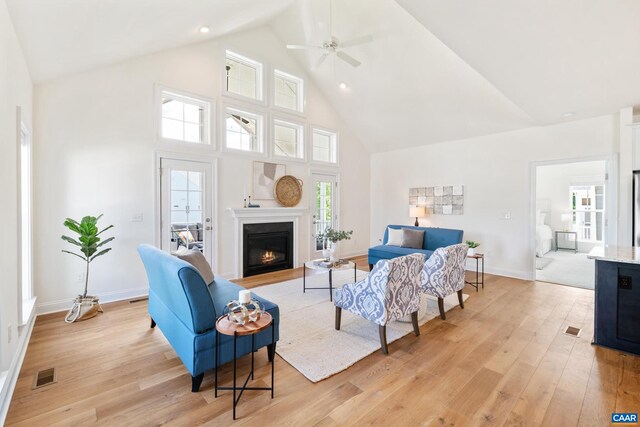 living room featuring high vaulted ceiling, light wood-style flooring, baseboards, and a glass covered fireplace