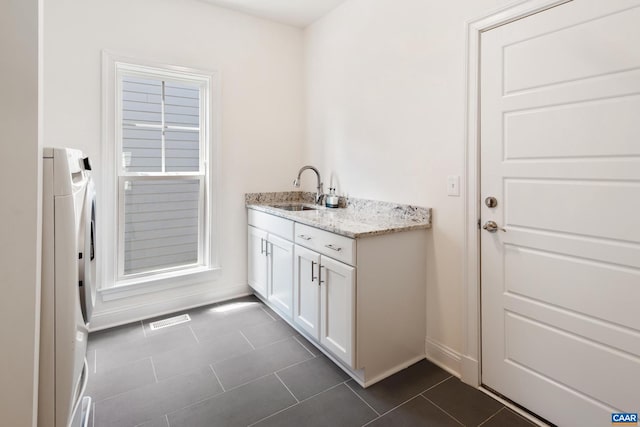 laundry area featuring washer / dryer, bar with sink, dark tile patterned flooring, and baseboards