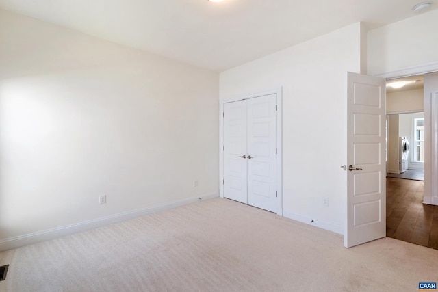 unfurnished bedroom with carpet, baseboards, a closet, and washer / dryer
