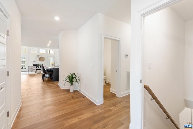 hall with an upstairs landing, light wood-type flooring, recessed lighting, and baseboards