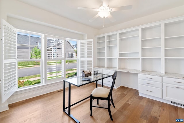 unfurnished office featuring built in desk, light wood finished floors, and a ceiling fan