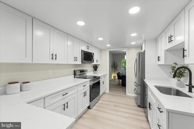 kitchen with appliances with stainless steel finishes, a sink, recessed lighting, white cabinets, and baseboards