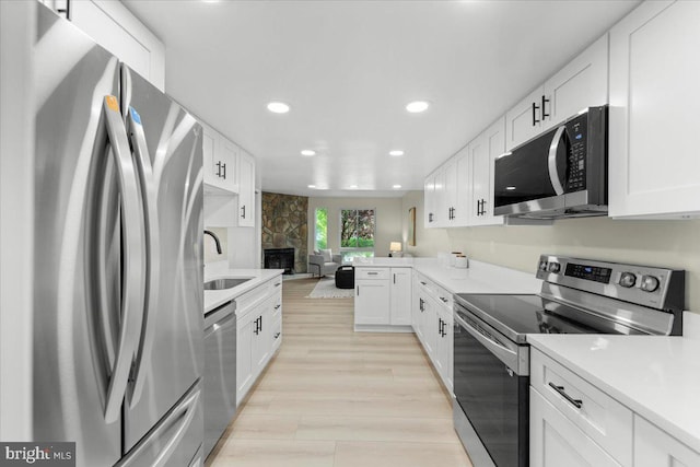 kitchen with appliances with stainless steel finishes, a sink, light countertops, light wood-style flooring, and white cabinetry