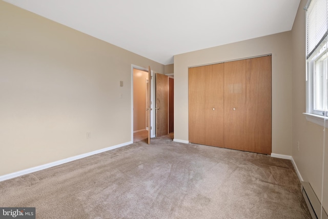 unfurnished bedroom with a baseboard radiator, carpet floors, baseboards, and a closet