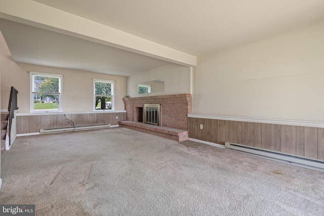 unfurnished living room with baseboard heating, carpet, wainscoting, a fireplace, and wooden walls