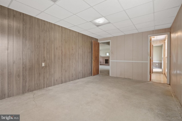 unfurnished room featuring a paneled ceiling, wooden walls, and concrete floors