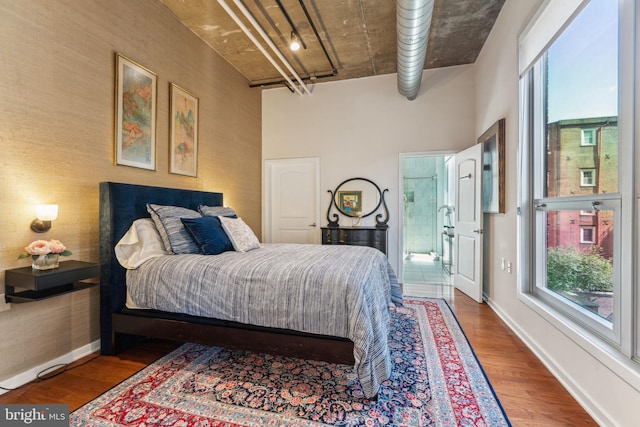 bedroom with wood finished floors, multiple windows, a towering ceiling, and baseboards
