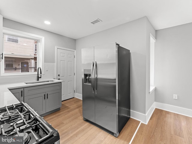kitchen with stainless steel fridge, range with gas stovetop, a sink, gray cabinetry, and light wood-style flooring