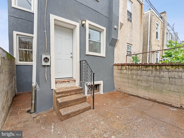 entrance to property featuring stucco siding and fence