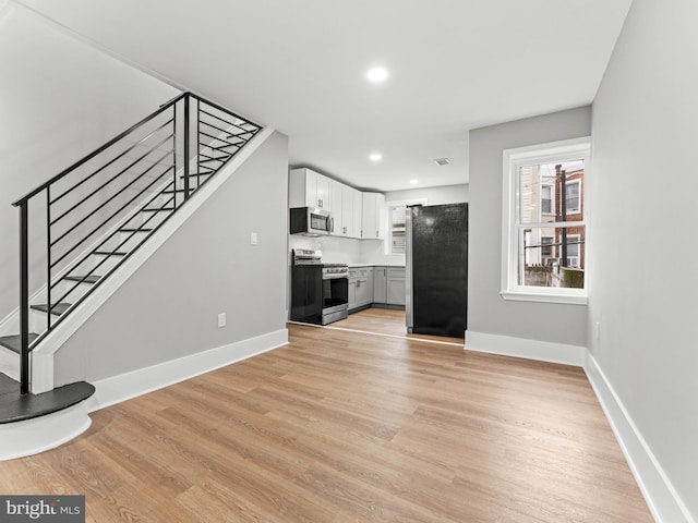 unfurnished living room featuring light wood-style floors, baseboards, stairway, and recessed lighting