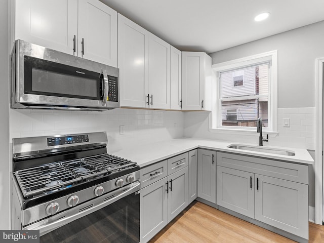 kitchen featuring appliances with stainless steel finishes, a sink, gray cabinets, light countertops, and light wood-style floors