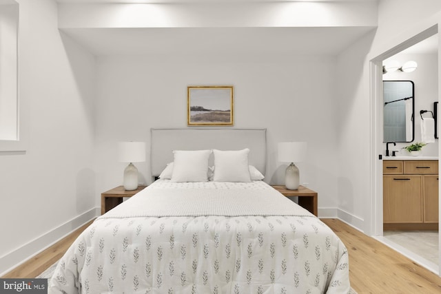 bedroom featuring light wood finished floors, baseboards, and ensuite bathroom
