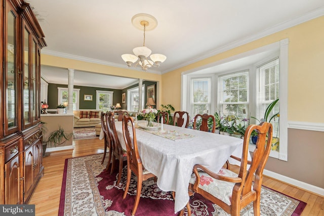 dining area featuring a chandelier, light wood finished floors, ornamental molding, baseboards, and ornate columns
