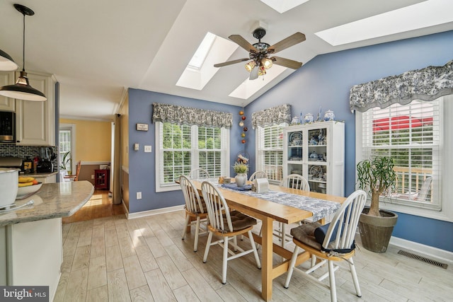 dining space featuring a skylight, light wood-type flooring, baseboards, and vaulted ceiling