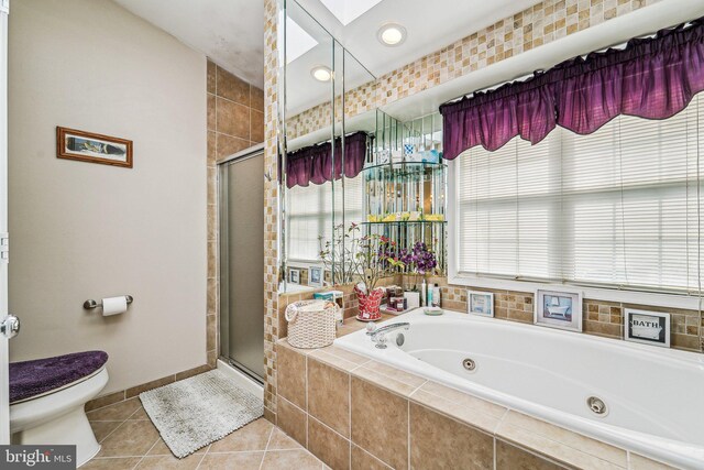 full bath featuring a shower stall, toilet, tile patterned flooring, a tub with jets, and a skylight