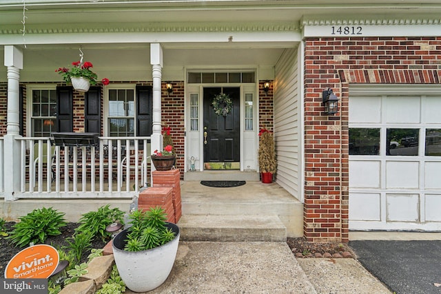 entrance to property featuring a porch, brick siding, and a garage
