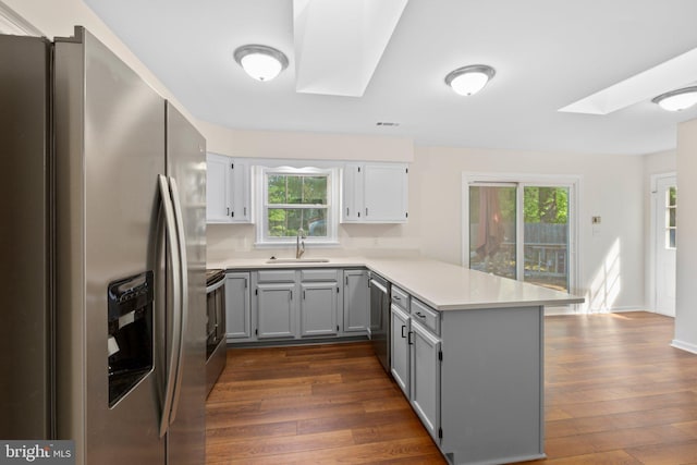 kitchen featuring stainless steel appliances, a skylight, a peninsula, a sink, and gray cabinetry