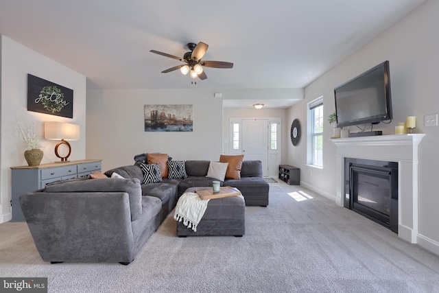living room featuring carpet floors, a ceiling fan, baseboards, and a glass covered fireplace