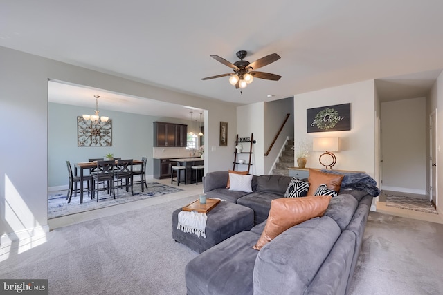 carpeted living area featuring stairs, a chandelier, ceiling fan, and baseboards