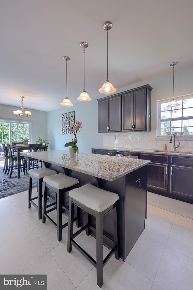 kitchen with a sink, decorative backsplash, light stone counters, light tile patterned floors, and a kitchen breakfast bar