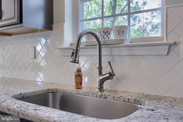 kitchen view of a sink, decorative backsplash, and light stone counters