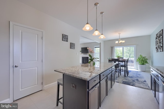kitchen with a chandelier, pendant lighting, a kitchen island, a breakfast bar area, and light stone counters