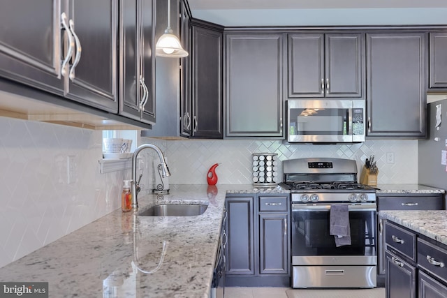 kitchen with stainless steel appliances, a sink, backsplash, light stone countertops, and hanging light fixtures
