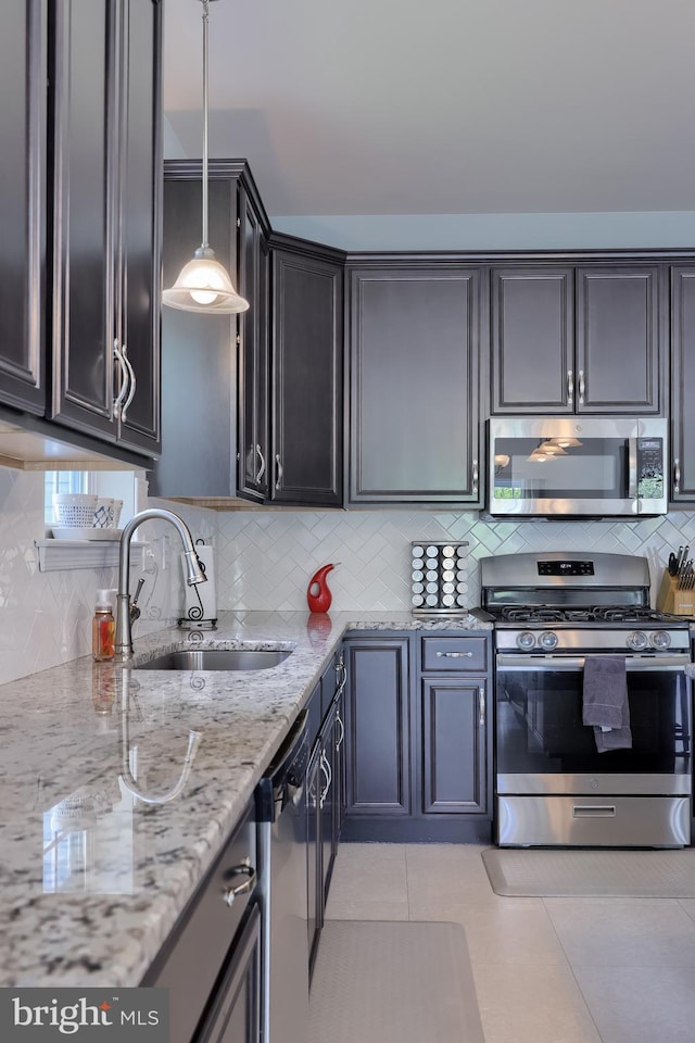 kitchen with stainless steel appliances, a sink, decorative backsplash, light stone countertops, and decorative light fixtures