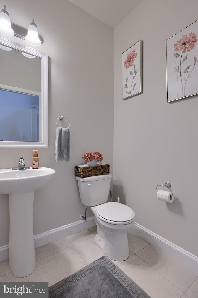 bathroom featuring baseboards, toilet, tile patterned floors, and a sink